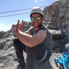 Climbing guide relaxing on the rocks, smiling with harness and helmet