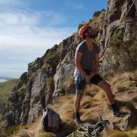 Man belaying at Cattelstop Crag with a dramatic cliffside and views over Christchurch and the Canterbury coastline