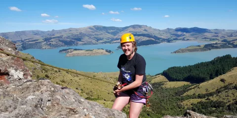 Woman abseiling with bright yellow helmet and Lyttelton Harbour in the background