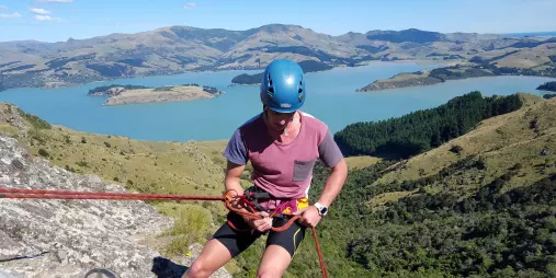 Climber preparing to abseil with rope over Lyttelton Harbour and rugged Banks Peninsula