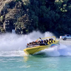 Yellow Alpine Jet boat speeds across turquoise water near Christchurch, creating a splash with passengers onboard