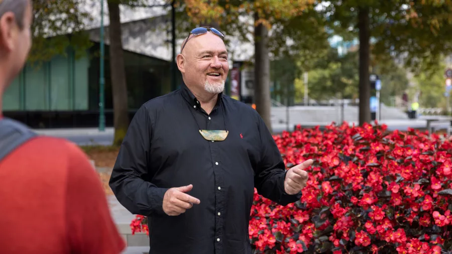 Māori guide leading a cultural tour in central Christchurch by a bed of red flowers