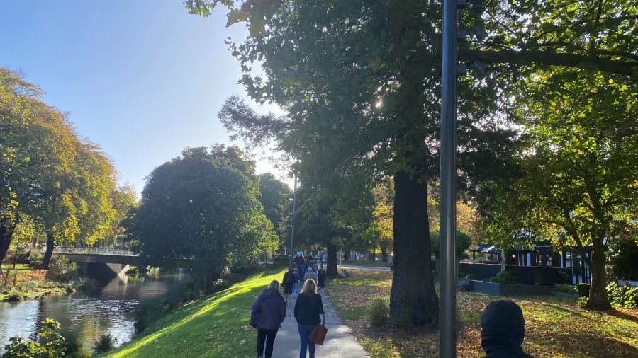 Group walking along the Ōtākaro River under autumn foliage