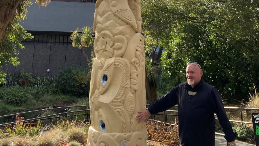 Māori guide from Amiki Tours standing beside a carved pou in Victoria Square, Christchurch