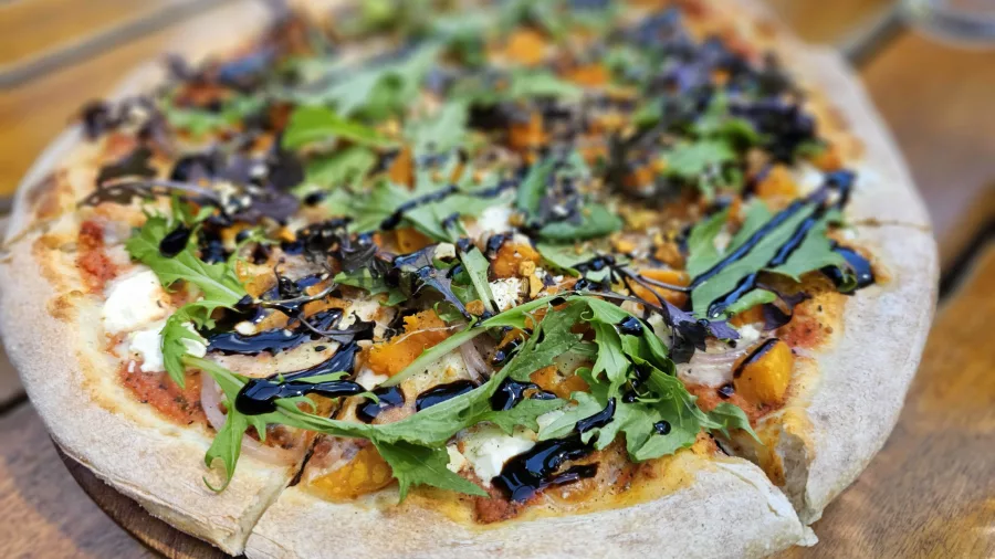 Close-up of a seasonal roast pumpkin pizza topped with greens and balsamic drizzle