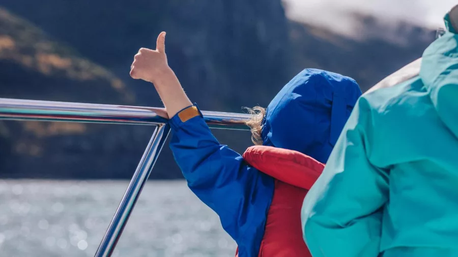 Child in a blue jacket and red life vest giving a thumbs up while on a dolphin cruise in Akaroa