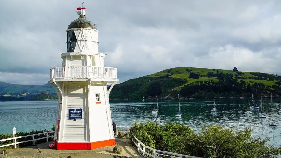 White wooden lighthouse overlooking the calm bay waters in Akaroa with sailing boats nearby