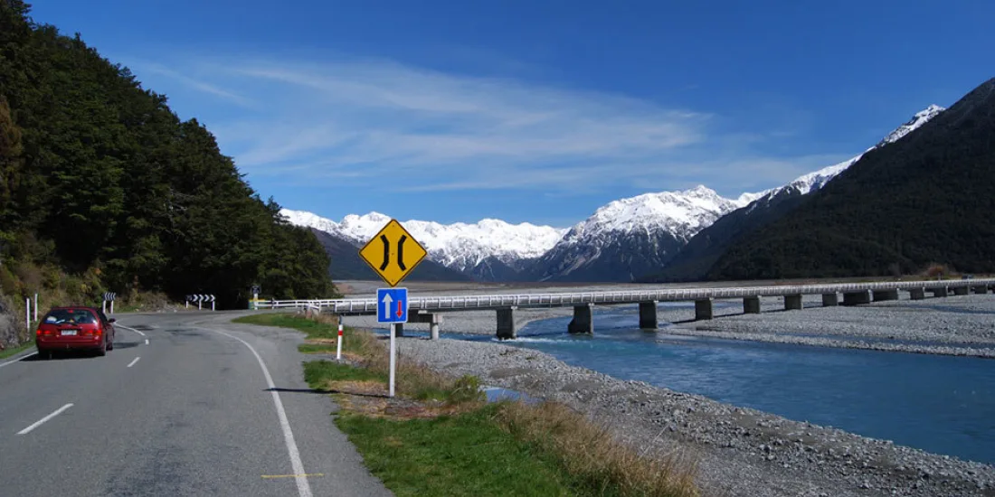 Scenic highway through Arthur’s Pass crossing the Bealey River with snowy mountains in the background