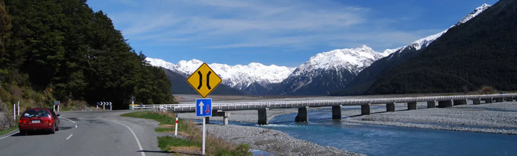 Scenic highway through Arthur’s Pass crossing the Bealey River with snowy mountains in the background
