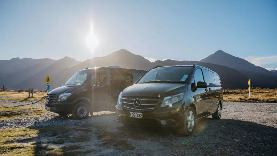 Tour vans parked with sunlit mountains in the background at Arthur’s Pass scenic stop