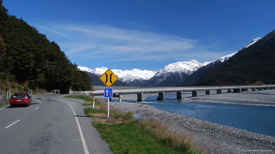 Scenic highway through Arthur’s Pass crossing the Bealey River with snowy mountains in the background