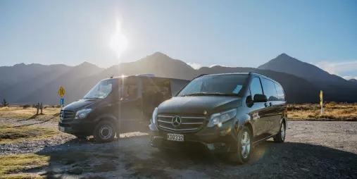 Tour vans parked with sunlit mountains in the background at Arthur’s Pass scenic stop