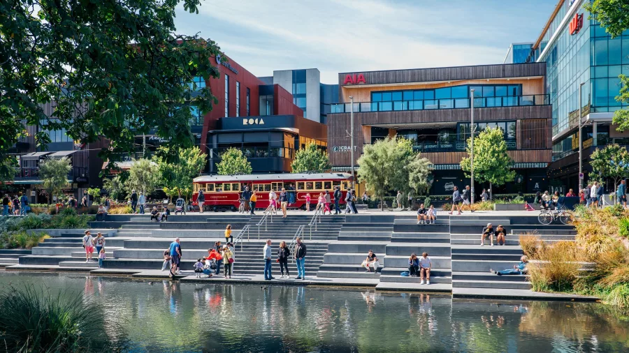 People relaxing by the Avon River in Christchurch with the historic tram and Riverside Market in the background