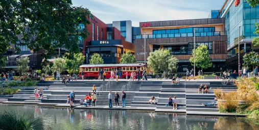 People relaxing by the Avon River in Christchurch with the historic tram and Riverside Market in the background