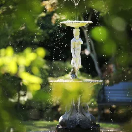 Decorative garden fountain with a classical statue surrounded by lush greenery