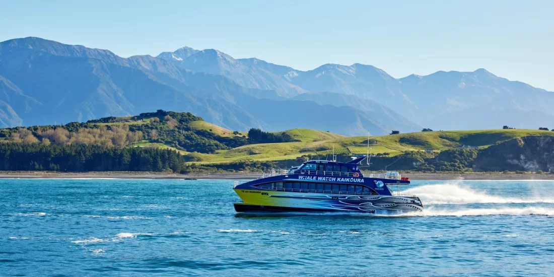 Whale Watch Kaikōura boat cruising with rolling green hills and the Seaward Ranges behind