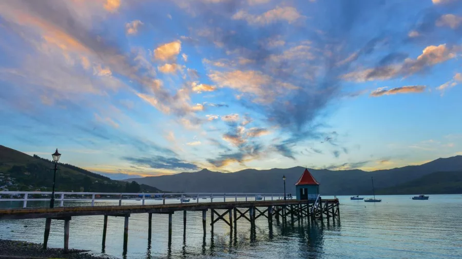 Wooden wharf at sunset in Akaroa Harbour with colourful skies and moored boats
