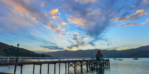 Wooden wharf at sunset in Akaroa Harbour with colourful skies and moored boats