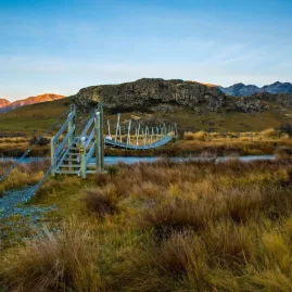 Swing bridge leading across a river to Mount Sunday at sunset, Canterbury, New Zealand