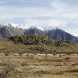 Rocky outcrop of Mount Sunday surrounded by dry tussock grass and mountain backdrop