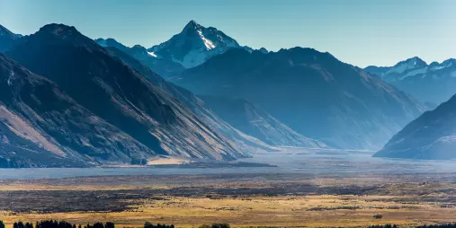 Mount Sunday rock formation with dry grasslands and dramatic snowy peaks in the background