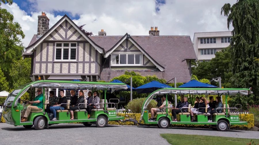 Electric shuttle parked in front of Curators House, a Tudor-style restaurant in Christchurch Botanic Gardens.