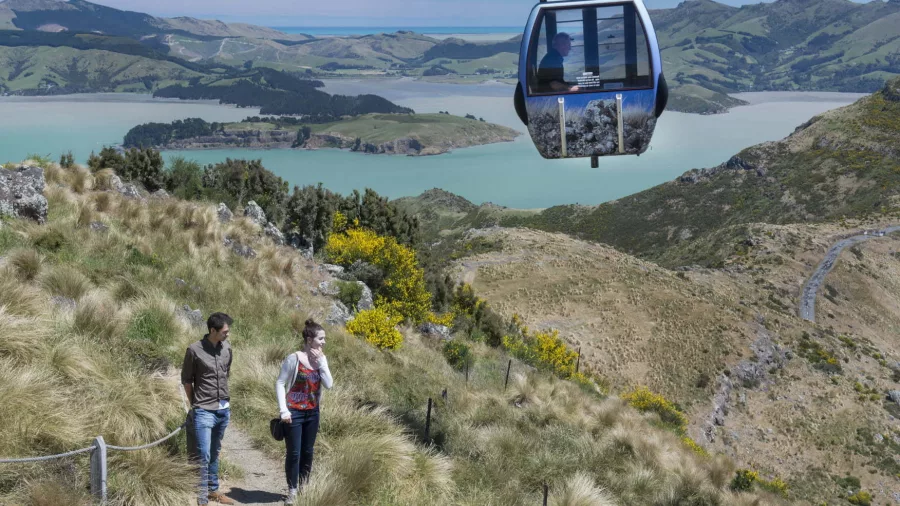 Two hikers walking near a Christchurch Gondola cabin with views of Lyttelton Harbour