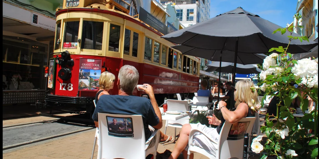 People enjoying outdoor dining on New Regent Street as a Christchurch heritage tram passes by.
