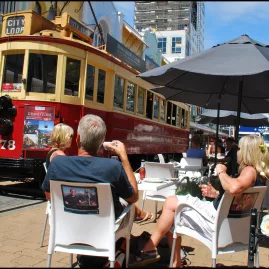 People enjoying outdoor dining on New Regent Street as a Christchurch heritage tram passes by.