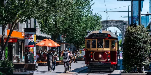 Historic red tram travelling through the Christchurch city centre with people dining and walking nearby