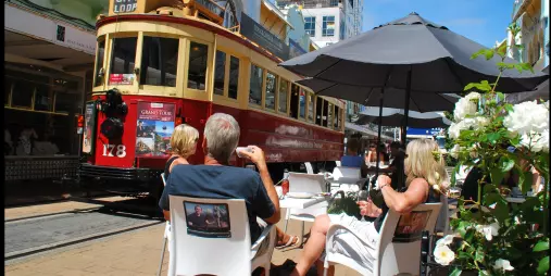 People enjoying outdoor dining on New Regent Street as a Christchurch heritage tram passes by.