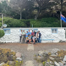 Group of walkers outside “Rosy Morn” bach at Boulder Bay, a historic coastal hut on Banks Peninsula