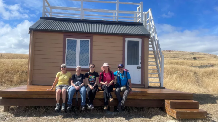 Hiking group sitting outside Scott’s Hut on the Crater Rim Walk near Godley Head