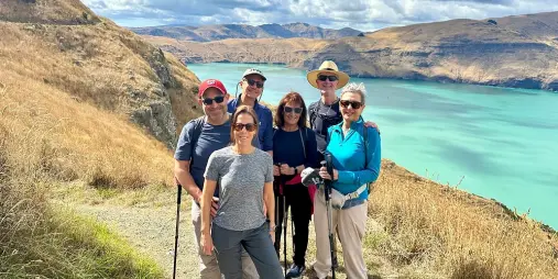 Group of six smiling hikers with stunning views of turquoise waters on the Crater Rim Walk