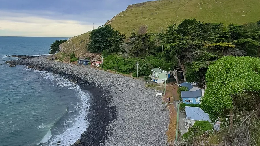 Elevated view over Boulder Bay showing pebbled beach and a row of small baches