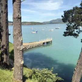 Sailboats moored near a wooden jetty in Corsair Bay, surrounded by calm turquoise water
