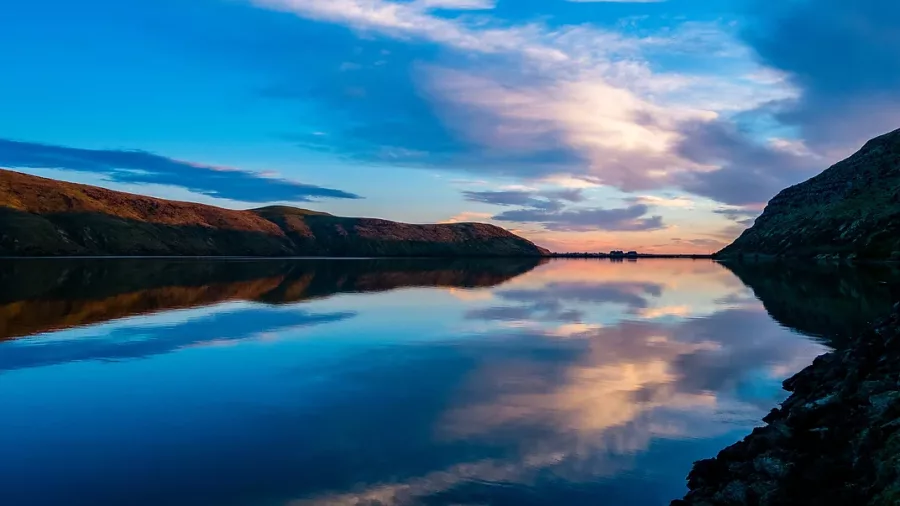 Calm water with mirror-like reflections of the sunrise and surrounding hills at Lyttelton Harbour