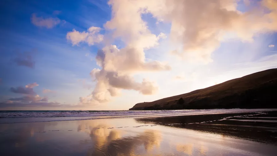 Sunset sky reflecting on the wet sand at Taylors Mistake Beach with headlands in the distance