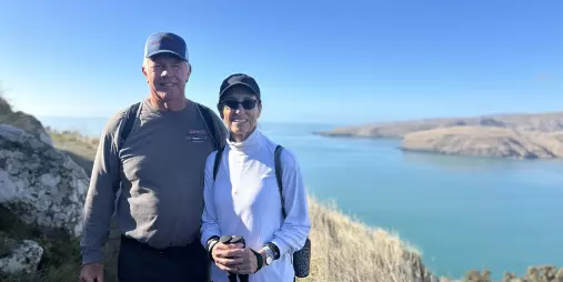 Couple standing on a clifftop track above Lyttelton Harbour on a sunny Crater Rim Walk