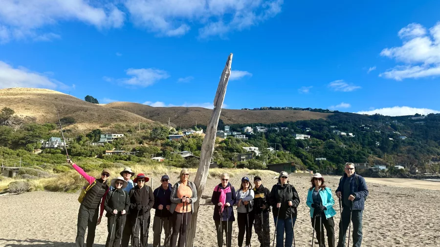 Large hiking group standing on the sand at Taylors Mistake Beach under a bright blue sky