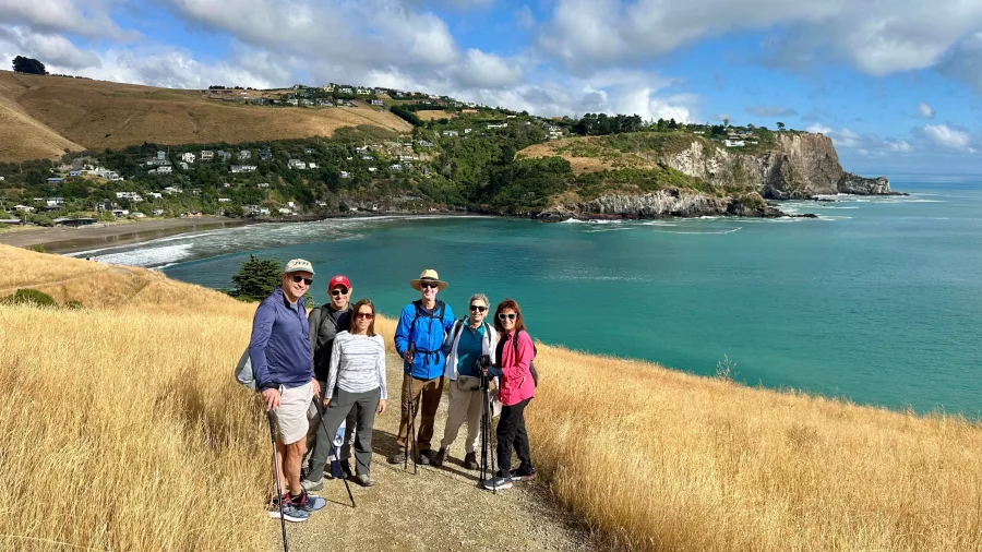 Group of hikers posing on a grassy coastal trail with Taylors Mistake beach and headland in the background