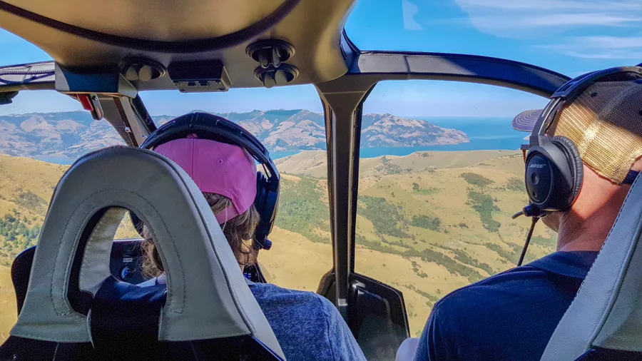 Passenger view from inside a helicopter flying over the hills towards Akaroa