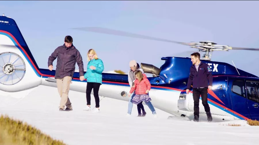 Family stepping out of a helicopter onto snow-covered mountains near Mount Cook