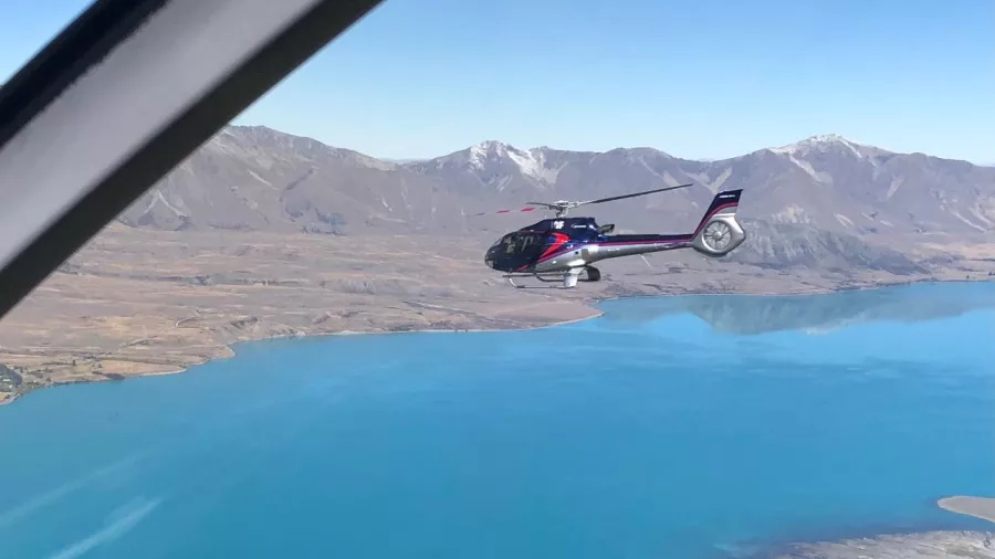 Helicopter flying over turquoise Lake Tekapo with alpine backdrop