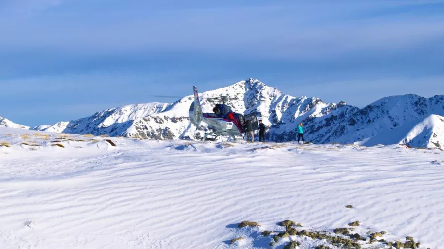 Helicopter landing on snowy mountain with passengers exploring the ridge