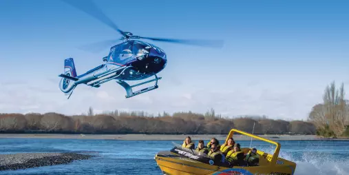Helicopter flying above jet boat on Waimakariri River