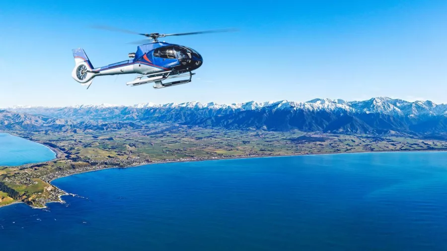 Helicopter over Kaikōura coast with mountain backdrop on whale watching tour