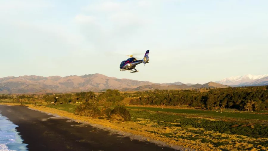 Helicopter flying along Kaikōura beach at golden hour