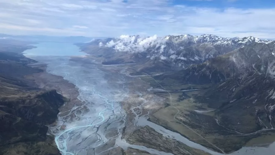 Aerial view of a braided river feeding into a turquoise lake with snow-capped mountains in the distance