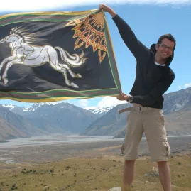 Smiling guest holding a Rohan flag with sweeping valley views near the Edoras filming site.